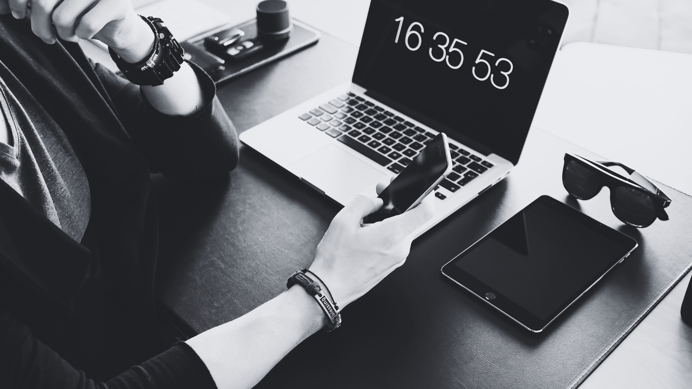 A hand using a mobile phone with other digital devices in the background